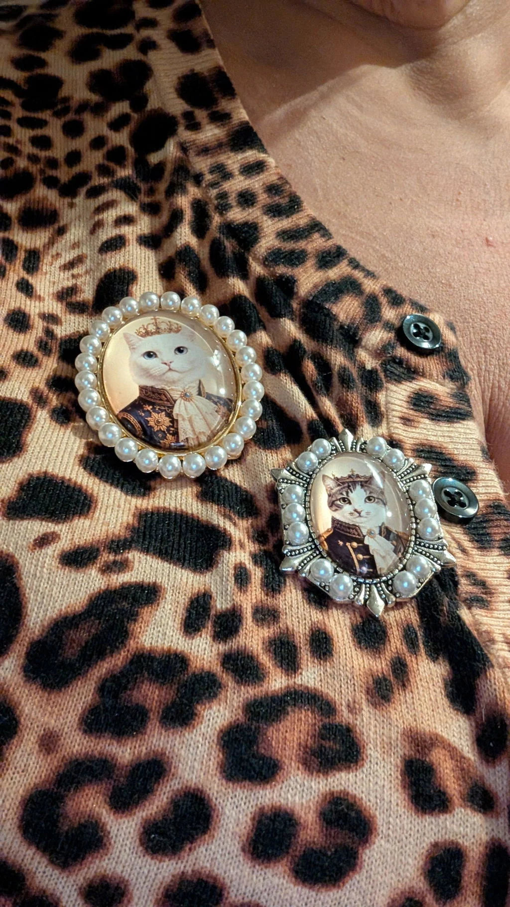 Two finished pearl-frame brooches with royal cat portraits worn on a cardigan
